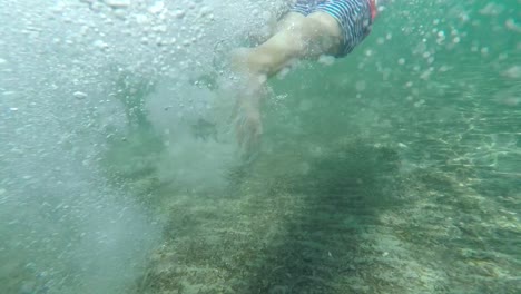 Underwater-slow-motion-shot-of-kid-swimming-and-creating-sparkles-and-bubbles-in-the-sea