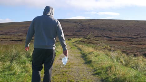 Sick-Man-Drops-His-Face-Mask-While-Walking-On-The-Mountain-Trail-In-Wicklow-Mountains,-Ireland---long-shot