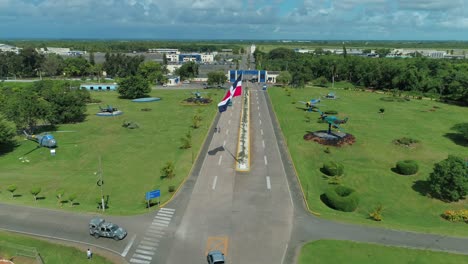 Entrance-of-the-military-air-base-of-san-isidro,-dominican-republic,-flag-waving-on-a-clear-day,-shot-with-drone