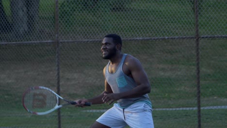 Bärtiger-Und-Muskulöser-Afroamerikanischer-Mann-Lacht,-Als-Er-Nach-Dem-Ball-Greift,-Der-Lässig-In-Zeitlupe-Tennis-Spielt