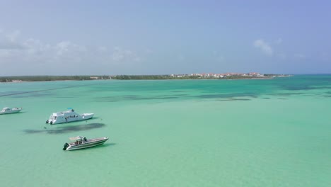 Luxury-white-boats-and-yacht-sit-in-clear-turquoise-exotic-Dominican-republic-ocean-waters,-Drone-Aerial