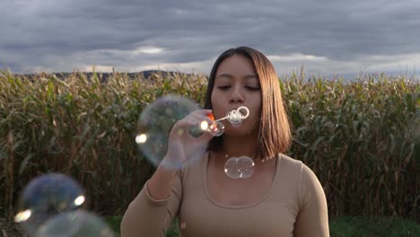 Pretty-woman-blowing-soap-bubbles-in-nature-during-sunlight-and-farm-field-in-background