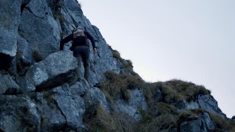 Hiker-climbs-up-big-boulders-under-a-cliff-at-dusk