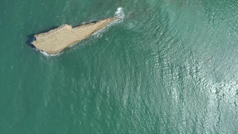 Aerial-shot-overlooking-the-rock-el-zapato-in-el-morro,-monte-cristi-waves-pounding,-blue-water