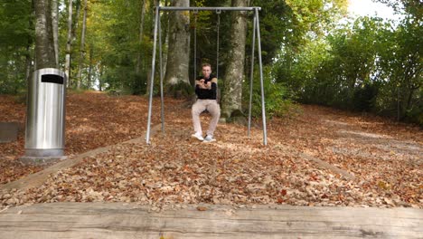 Young-man-swaying-and-jumping-from-swing,landing-on-falling-leaves-in-forest-during-autumn