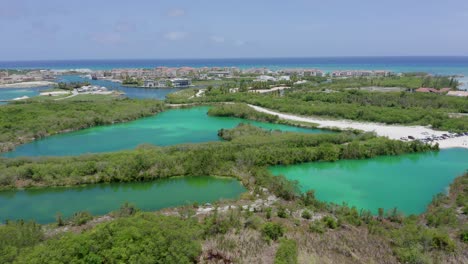 Backward-flight-showing-cap-cana-marina-from-blue-lake,-sunny-afternoon,-green-water,-nice-weather
