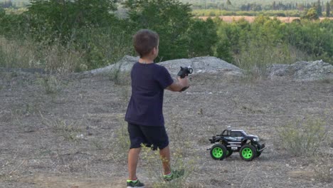 Slow-motion-of-caucasian-kid-playing-with-his-RC-car-toy-in-the-fields,-moving-backwards