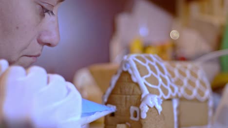 Close-up-on-caucasian-woman,-decorating-a-gingerbread-cookie-house-for-christmas,blurry-background-4K