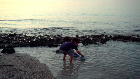 Artistic-shot-of-caucasian-boy,-wetting-his-feet,-and-playing-at-the-beach,-late-evening-with-beautiful-colours-4K