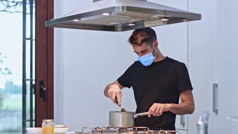 Young-man-at-home-preparing-food-with-protective-mask