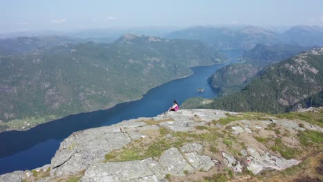 Norwegian-girl-in-the-mountain,-looking-down-at-remote-fjord-in-amazing-scenery