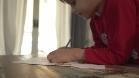 Caucasian-boy-painting-a-magic-lamp-draw-using-a-yellow-marker-indoors,-side-view,-natural-light-from-window-in-the-background-4K