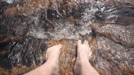 Male-dipping-toes-in-river-water-over-whitewater-rocks,-closeup