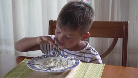 Caucasian-tanned-kid,-sitting-at-house's-table-eating-rice-and-playing-with-it-4K