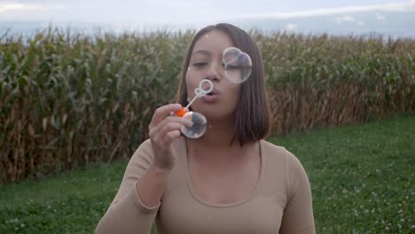 Young-woman-blowing-bubbles-on-agriculture-field-during-cloudy-day-in-nature