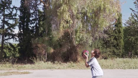Kaukasischer-Junge-Spielt-Basketball-Auf-Dem-Korbplatz-Der-Gasse,-Hohe-Bäume-Im-Hintergrund,-Zeitlupe