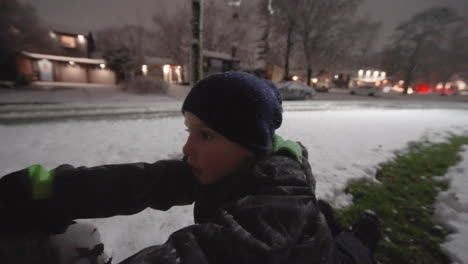 Close-up-little-boy-rolling-a-large-snowball-on-a-winter-evening