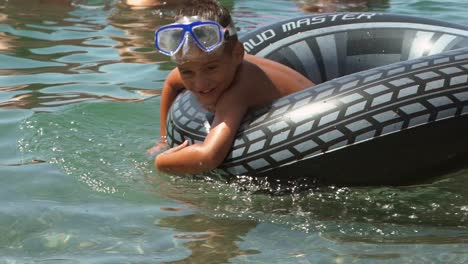 Medium-shot-of-caucasian-toddler-boy,-enjoying-the-sea-wearing-sun-mask-and-using-an-inflatable-ring-to-swim,-slow-motion