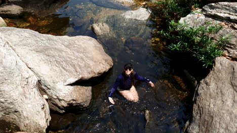 Young-Latin-woman-in-swimwear-wading-in-rocky-natural-pool,-medium-down-shot