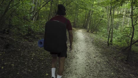 A-young-latino-is-walking-a-forest-path-with-a-yoga-mat-in-his-hand
