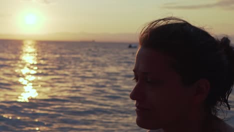 Close-up-on-caucasian-greek-woman's-face,-with-beautiful-sunset-at-sea-of-Kalamata,-Peloponnese-,-Greece