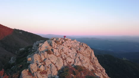 Parallax-drone-shot-of-a-woman-doing-yoga-on-top-of-a-mountain-with-the-first-lights-of-sunrise