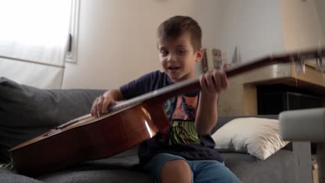 Caucasian-four-years-old-boy,-tying-to-play-a-classic-guitar-at-home-4K-30fps