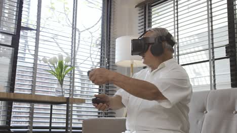 Asian-old-man-grey-hair-playing-Virtual-Reality-VR-enjoying-video-games-cheerful-on-a-sofa-in-the-living-room-at-home