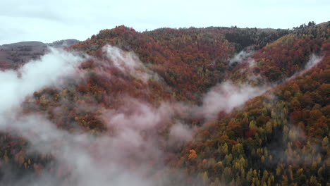 Aerial-view-Drone-flying-through-clouds-revealing-autumn-color-forest-hills,-establishing-shot