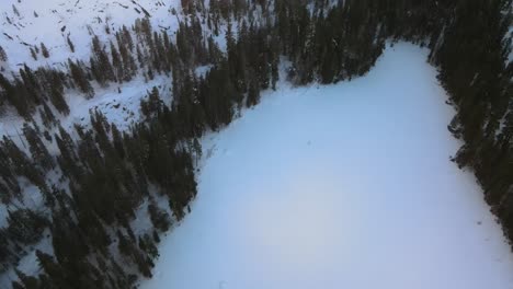 Drone-birdseye-footage-over-snowy-alpine-forest-and-frozen-lake-in-Lake-Tahoe,-USA