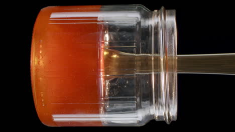Vertical-video-close-up-of-a-honey-jar-getting-filled-with-honey