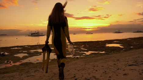 Woman-with-snorkeling-gear-walking-into-the-ocean-at-sunset