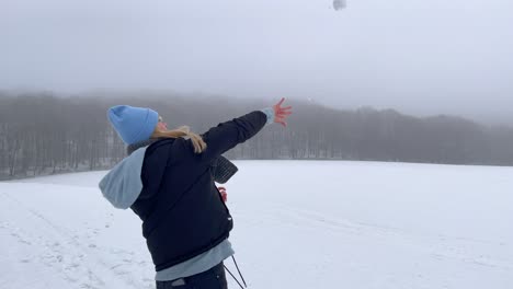 Slow-motion-shot-of-attractive-young-woman-throwing-snowball-in-the-air-during-beautiful-snowy-cold-winter-day-with-forest-and-fog-in-background
