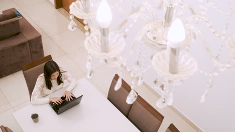 Down-shot-of-Caucasian-woman-working-from-home-on-laptop,-under-chandelier