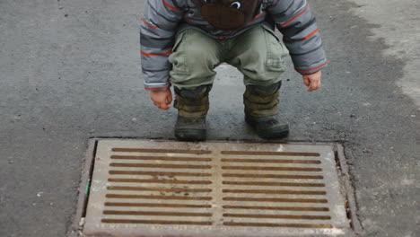 Curious-toddler-boy-looking-down-a-storm-drain
