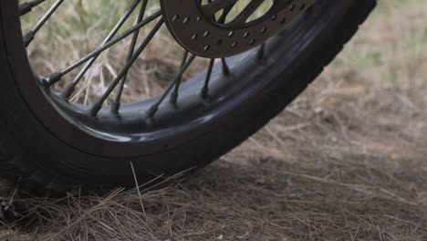 Close-up-on-motorcycle-wheels,-static-on-soil-ground,-low-ground-view-pan-movement-120fps