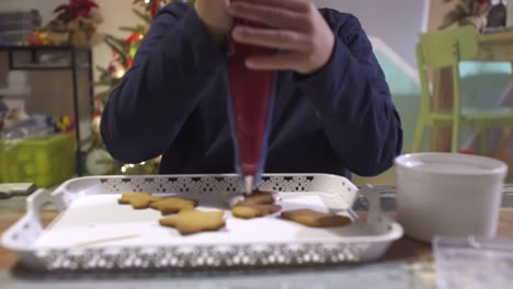 Nahaufnahme-Auf-Kaukasischem-Kind,-Weihnachtshausgemachte-Lebkuchenplätzchen-Mit-Roter-Zuckerglasur-Dekorierend,-Mit-Spritzbeutel
