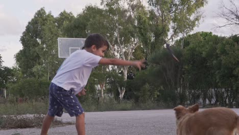 Cauacasian-toddler-boy,-throws-a-plastic-toy-stick-at-his-pet-dog-outdoors,-slow-motion