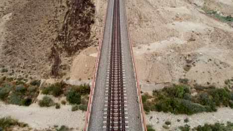 aerial-forward-slow-drone-shot-of-an-empty-train-rail-bridge,-revealing-the-desert-in-day-light