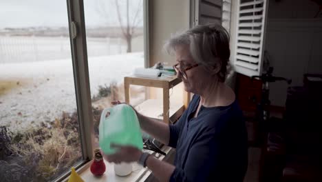 Mature-woman-mixes-the-fertilized-and-balanced-water-for-her-hydroponics-indoor-garden-with-snow-outside