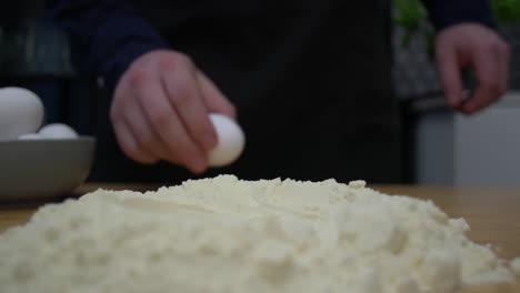 Breaking-an-egg-open-and-pouring-whites-and-yolk-into-pile-of-flour---Eye-level-close-up-slow-motion-shot