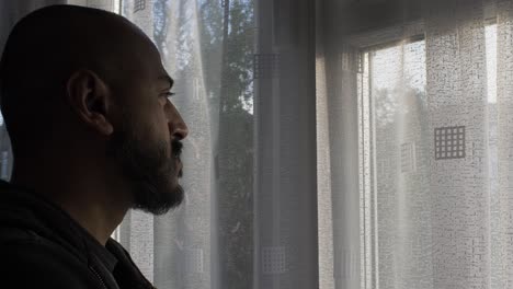 Ethnic-UK-Asian-Male-Looking-Out-Of-Window-In-Pensive-Mood-During-Locked-Down
