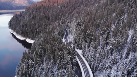 Aerial-cinematic-view-of-car-drive-on-a-forest-road-in-winter-with-snow-on-top