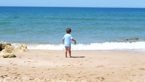 Kleiner-Junge,-Der-An-Einem-Sandstrand-Durch-Die-Wellen-Des-Ozeans-Geht-Und-Spielt