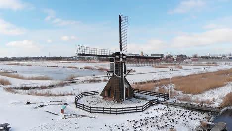 Windmill-in-winter-snow-scene,-Netherlands-landscape,-rising-aerial-view