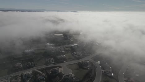 Drone-footage-through-cloud-line-on-a-misty-morning,-showing-Folsom,-USA-in-breaks-through-the-clouds-revealing-a-neighborhood-below