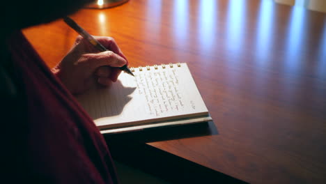 Middle-aged-caucasian-woman-with-aging-hands-writing-an-old-fashioned-paper-and-pen-mail-letter-or-handwritten-note-to-a-friend-on-a-wooden-desk