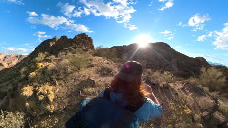Sun-flares-burst-over-red-haired-hiker-crests-a-hill-in-a-rocky-mountain-desert