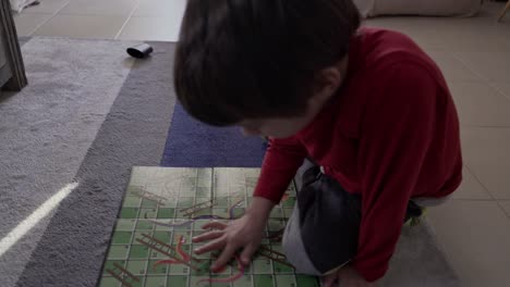 Top-view-of-caucasian-boy-,-playing-classic-board-game-Snakes-and-Ladders-on-the-carpet-at-living-room-indoors