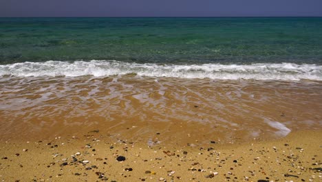 Sanfte-Wellen-Waschen-Sich-An-Einem-Goldenen-Strand-Mit-Kleinen,-Glatten,-Verstreuten-Steinen